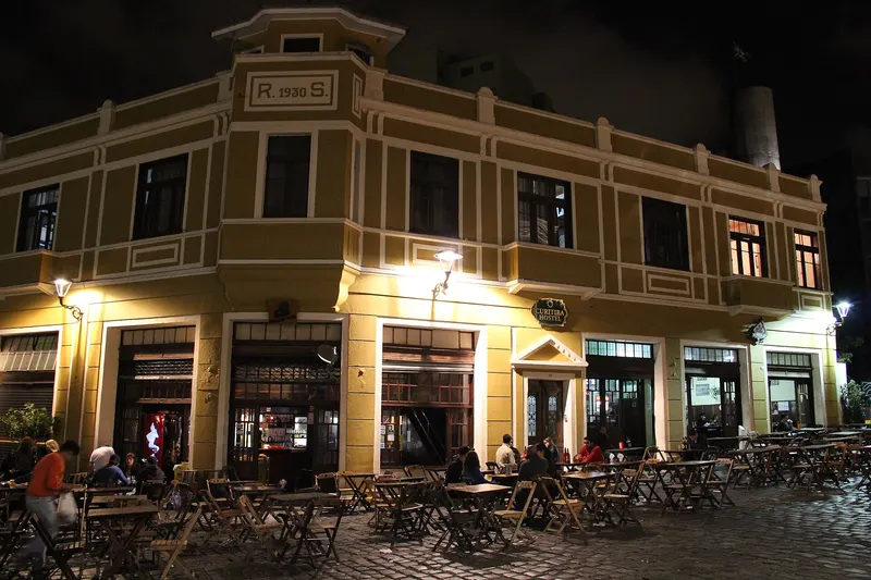 Bares do Largo da Ordem à noite, com mesas na calçada de pedra em frente a um casarão iluminado