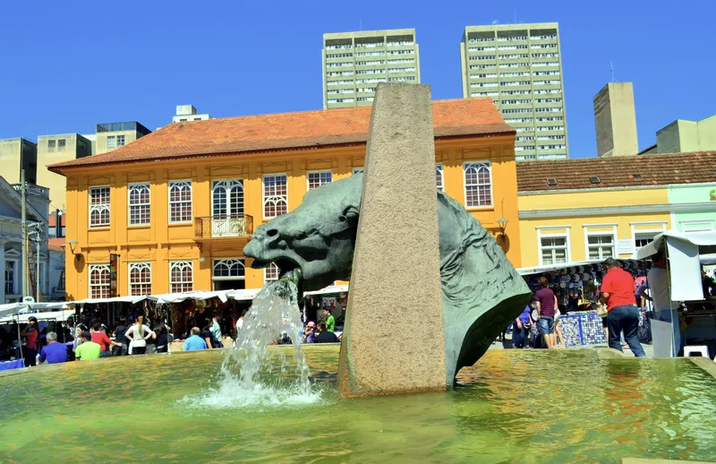 Domingo de feira no Largo da Ordem, com o chafariz do Cavalo Babão, barracas e um casarão amarelo